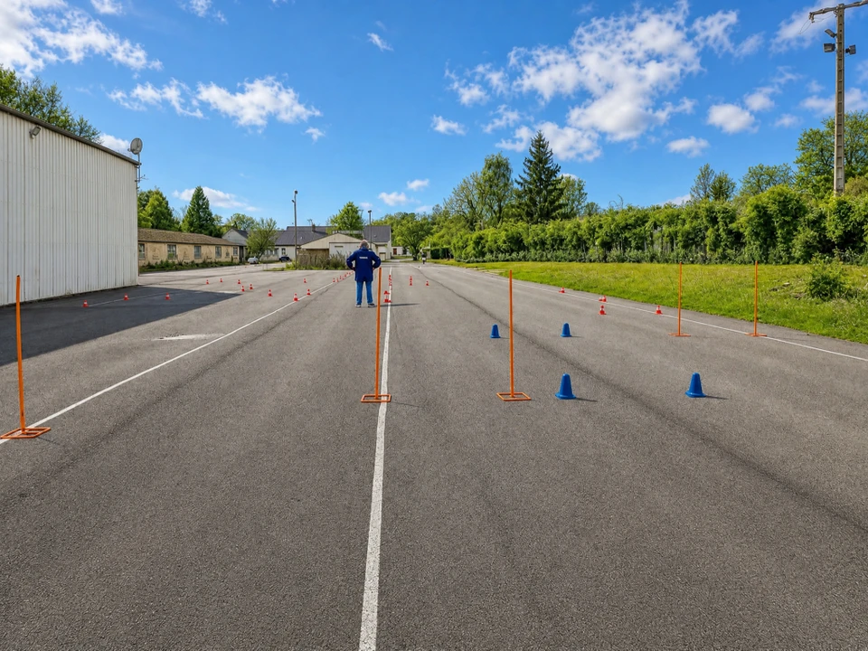 Piste d'entraînement extérieure balisée avec des cônes de signalisation bleus et orange, des jalons verticaux oranges sur socles et des cônes rouges et blancs